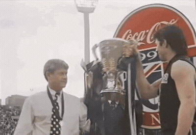 Two Men Holding Trophy In Front Of Coca-Cola Sign GIF