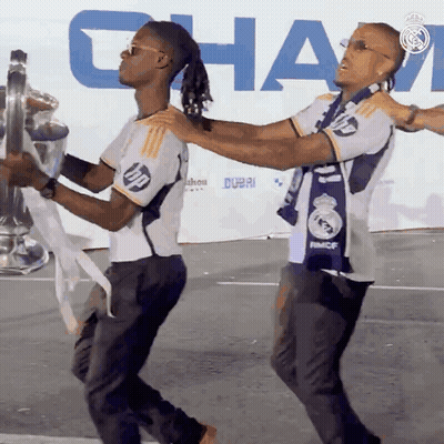 Two Men Holding Trophy In Front Of Dubai Sign GIF