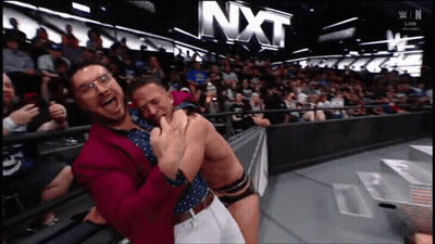 Two Men Hugging In Front Of NXT Sign GIF