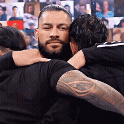 Two Men Hugging In Front Of Wall Of Pictures GIF