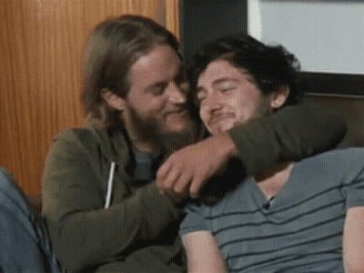 Two Men Hugging On Couch One Smiling GIF