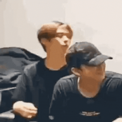 Two Men In Baseball Caps Sitting Together GIF