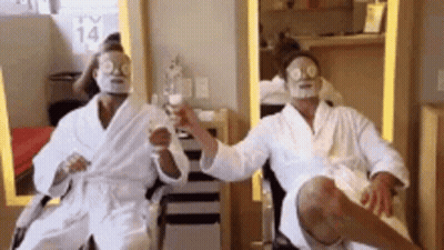 Two Men In Bathrobes With Face Masks On Their Faces Are Sitting In A Chair . GIF