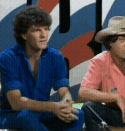 Two Men In Blue And Pink Shirts Sitting GIF