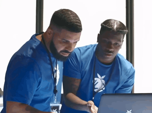 Two Men In Blue Shirts Are Looking At A Laptop Computer GIF