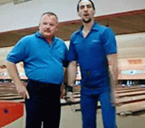 Two Men In Blue Shirts Are Posing For A Picture In A Bowling Alley GIF