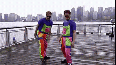 Two Men In Colorful Overalls Dancing On Pier GIF