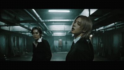 Two Men In Dark Room One With Long Hair GIF