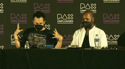 Two Men In Face Masks Sitting In Front Of Pax Unplugged Sign GIF