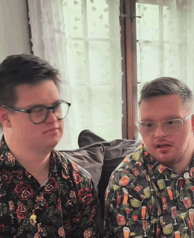 Two Men In Glasses And Drink Shirts Sitting Together GIF