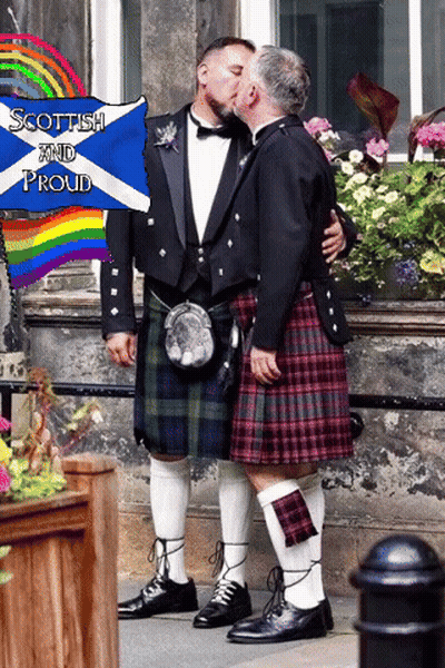 Two Men In Kilts Kiss In Front Of A Sign That Says " Scottish And Proud " GIF