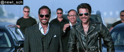 Two Men In Leather Jackets And Sunglasses Smiling Near Cars GIF