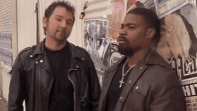 Two Men In Leather Jackets Are Standing Next To Each Other In Front Of A Wall Covered In Posters . GIF