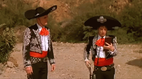 Two Men In Mariachi Outfits Are Standing Next To Each Other On A Dirt Road GIF