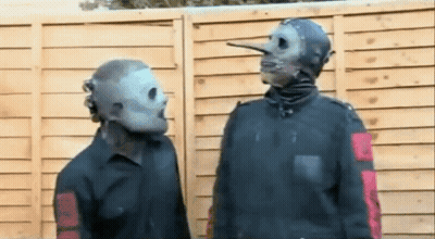 Two Men In Masks Standing In Front Of Wooden Fence GIF
