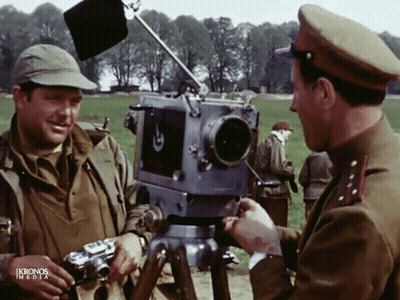 Two Men In Military Uniforms Talking In Front Of Kronos Media Camera GIF