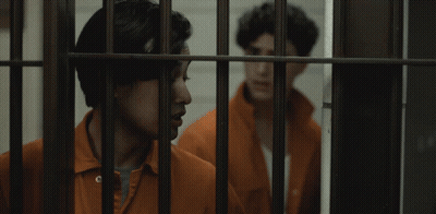 Two Men In Orange Jumpsuits Behind Bars GIF