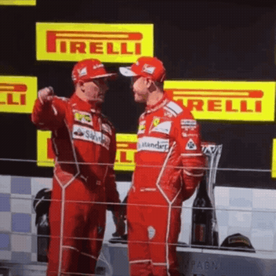 Two Men In Red Ferrari Uniforms Are Standing Next To Each Other On A Podium GIF
