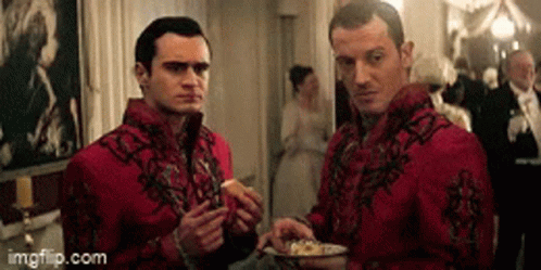 Two Men In Red Jackets Are Standing Next To Each Other In A Room Eating Food . GIF