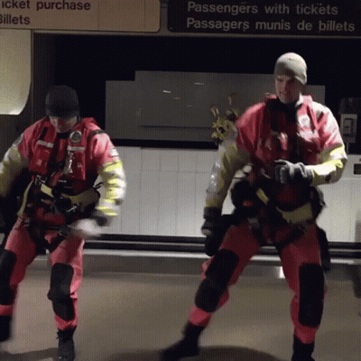 Two Men In Safety Suits Are Dancing In Front Of A Sign That Says Passengers With Tickets GIF