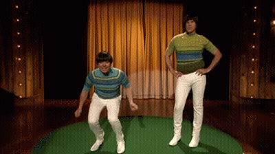 Two Men In Striped Shirts And White Pants Are Jumping In The Air On A Stage GIF