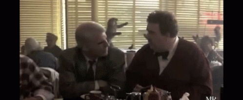 Two Men In Suits And Bow Ties Are Sitting At A Table In A Diner Talking To Each Other . GIF