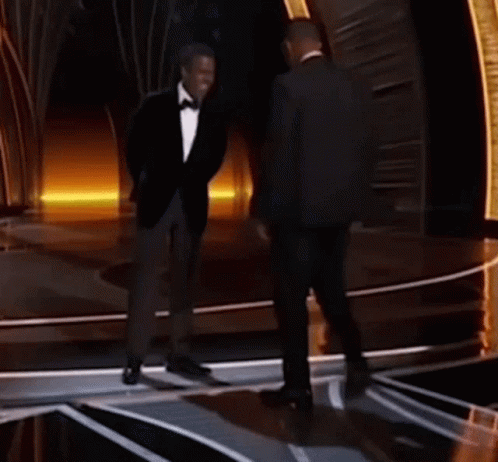 Two Men In Suits And Bow Ties Are Standing On A Stage Talking Into Microphones . GIF