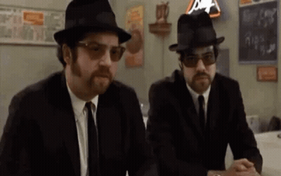 Two Men In Suits And Hats At Table GIF