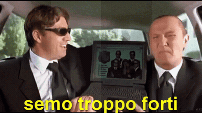 Two Men In Suits And Ties Are Sitting In A Car And One Is Holding A Laptop With A Picture Of A Group Of Men On It GIF