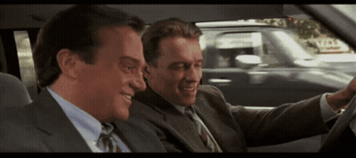 Two Men In Suits And Ties Are Sitting In A Car And One Of Them Is Smiling GIF