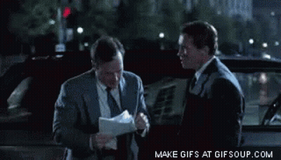 Two Men In Suits And Ties Are Standing Next To Each Other In Front Of A Car And Looking At Papers GIF