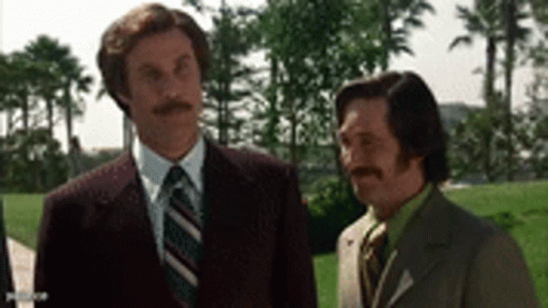 Two Men In Suits And Ties Are Standing Next To Each Other In Front Of Palm Trees . GIF