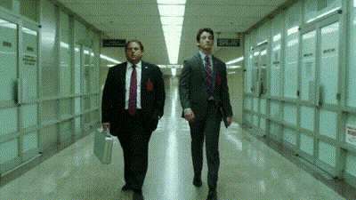 Two Men In Suits And Ties Are Walking Down A Hallway With A Sign On The Wall That Says " No Smoking " GIF