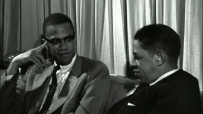 Two Men In Suits And Ties Sitting Next To Each Other GIF