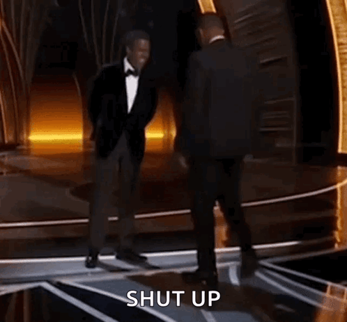 Two Men In Suits Are Dancing On A Stage And The Words Shut Up Are Visible Behind Them . GIF