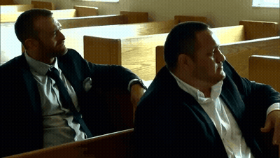 Two Men In Suits Are Sitting In A Church Talking GIF