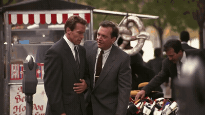 Two Men In Suits Are Standing In Front Of A Hot Dog Stand GIF
