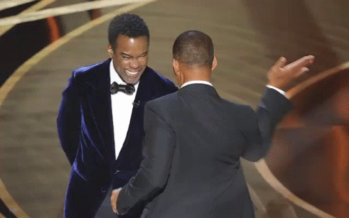 Two Men In Suits Are Standing Next To Each Other On A Stage And Shaking Hands . GIF