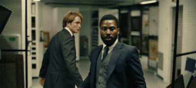 Two Men In Suits Are Walking Down A Hallway And One Has A Beard GIF