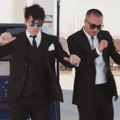 Two Men In Suits Dancing In Front Of A Gas Pump That Says Notice On It GIF