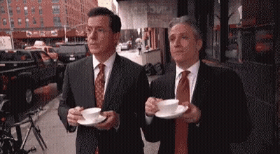 Two Men In Suits Holding Coffee On City Street GIF