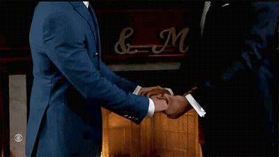 Two Men In Suits Shaking Hands In Front Of Fireplace With Sign & N GIF