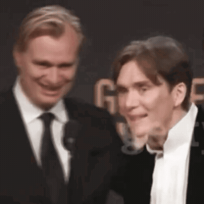 Two Men In Suits Smiling On Red Carpet GIF