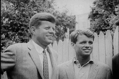 Two Men In Suits Standing By Fence GIF