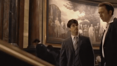 Two Men In Suits Standing In Front Of Painting GIF
