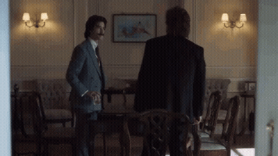 Two Men In Suits Standing In Room With Chairs GIF