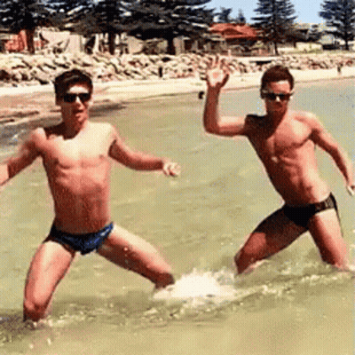 Two Men In Swim Trunks Are Standing In The Water . GIF