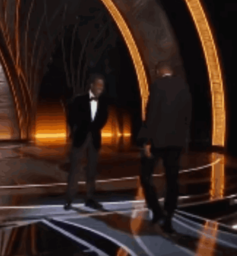 Two Men In Tuxedos Are Dancing On A Stage At An Event GIF