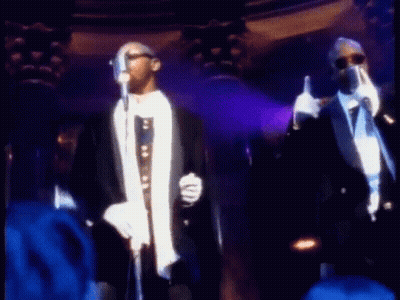 Two Men In Tuxedos Are Singing Into Microphones On Stage . GIF