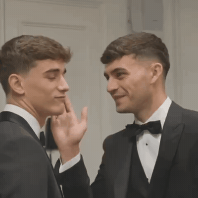 Two Men In Tuxedos Are Standing Next To Each Other And Touching Their Faces . GIF